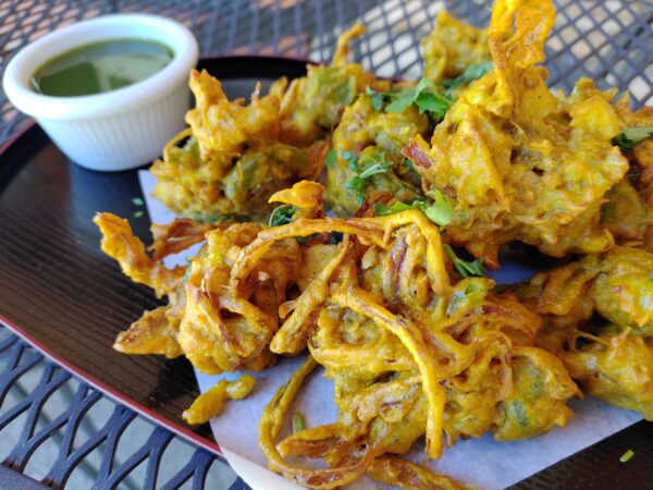 Mixed Vegetable Pakora Fritter originating from the Indian subcontinent, consists of vegetables such as potatoes and onions, coated in seasoned gram flour batter and deep fried. Served with Green Chutney